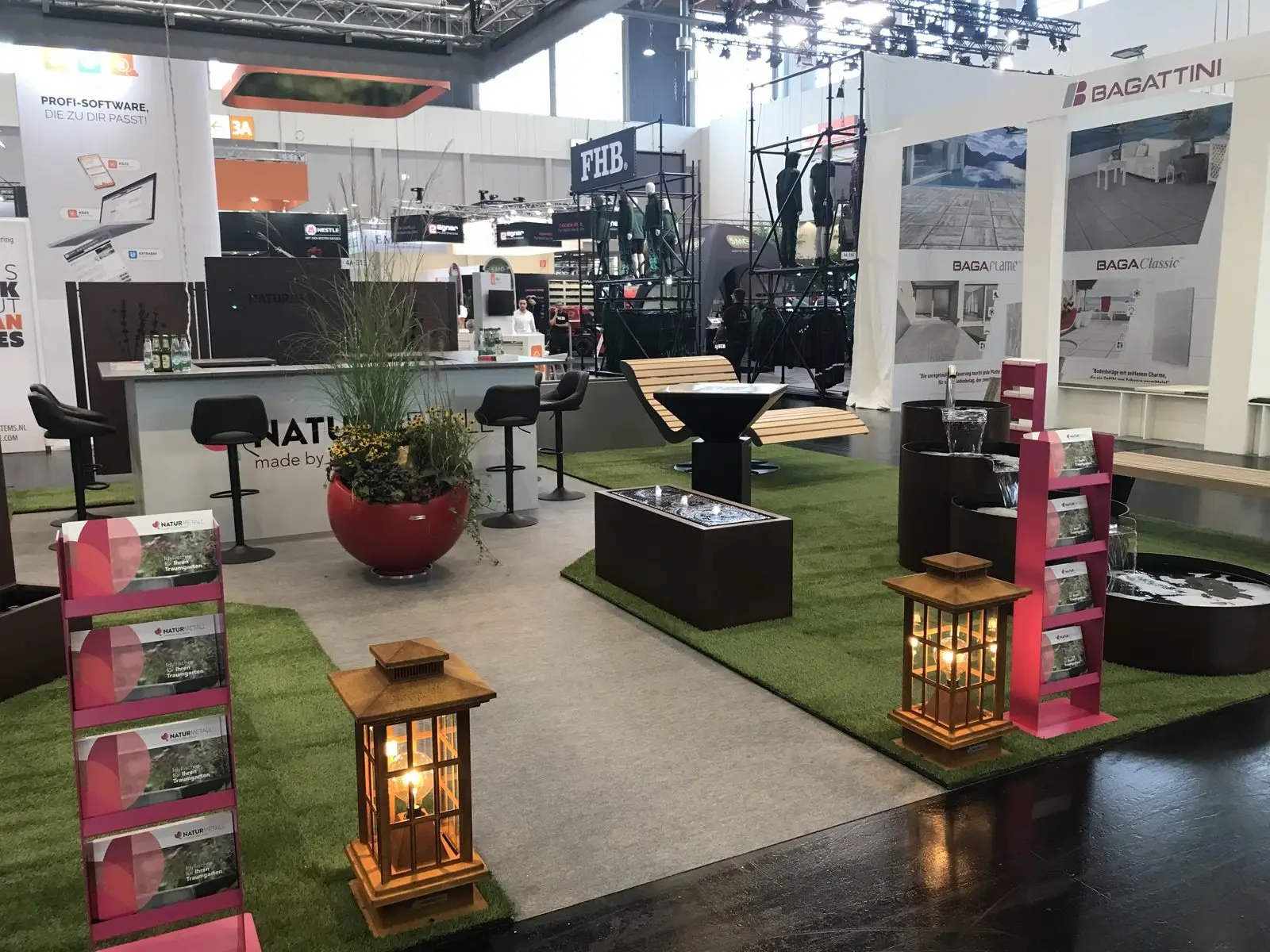 Messestand von naturmetall auf der GaLaBau 2024 mit Theke, rotem Kugelpflanzgefäß, Wasserelementen, Gartenlaternen und Prospektständern