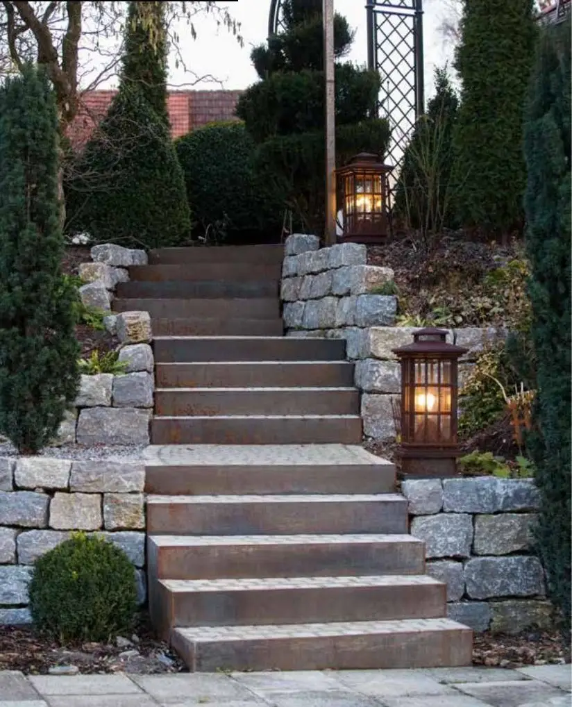 Treppe aus Cortenstahl zwischen Natursteinmauern mit zwei Gartenlaternen